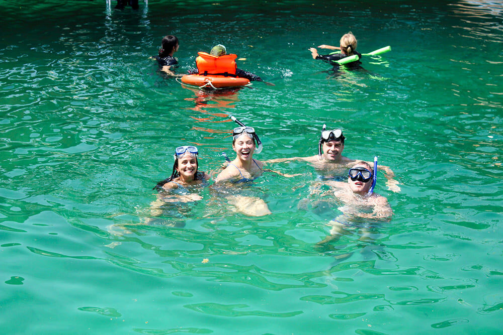 Tourists snorkeling in turquoise waters next to a traditional Omani dhow at historic Telegraph Island Khasab Musandam