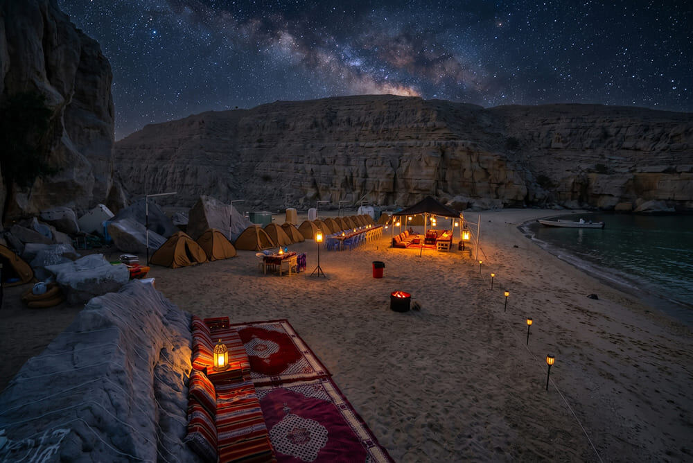Campsite with illuminated dome tents and beach campfire on a secluded Musandam fjord beach